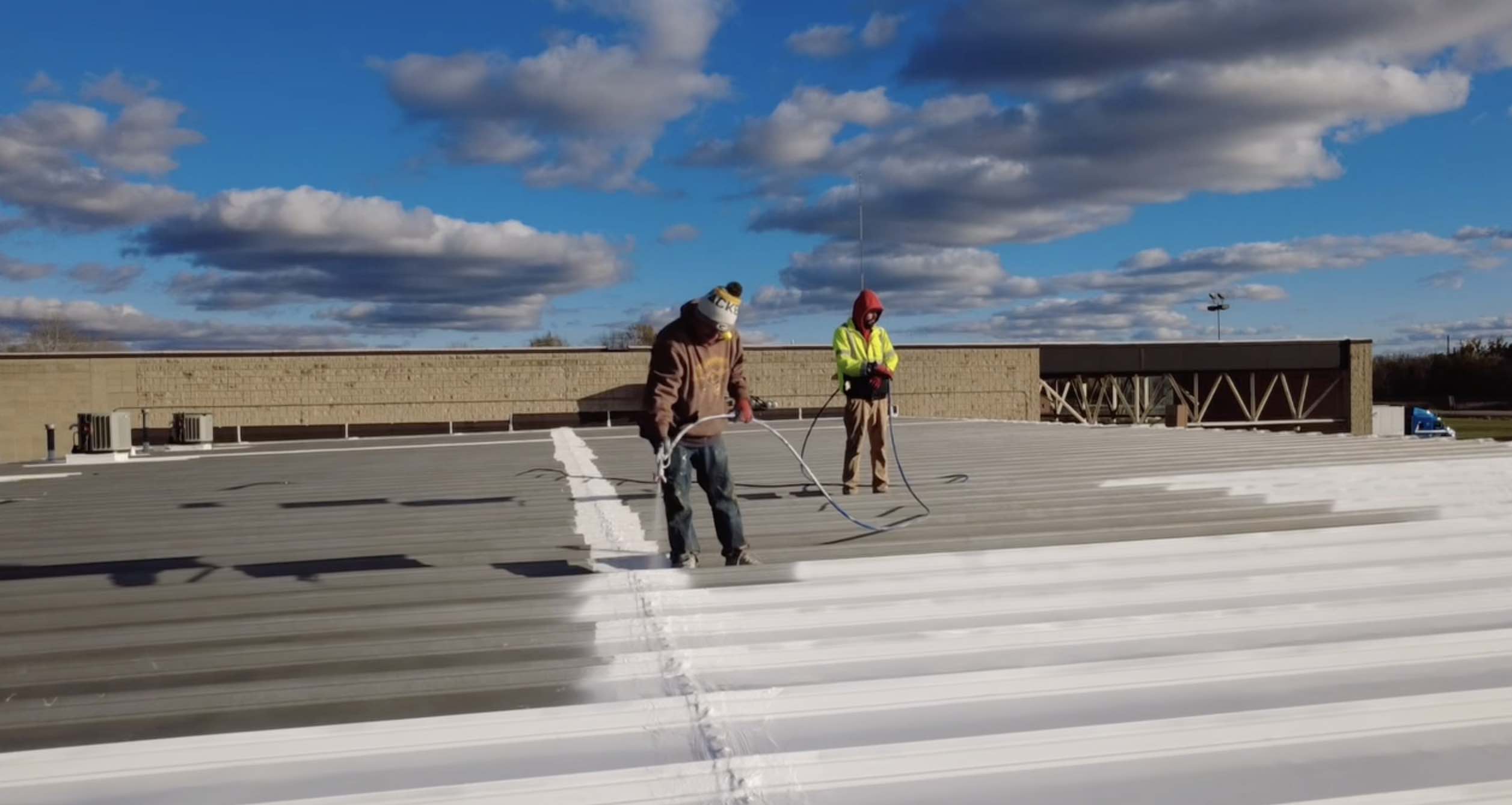 Two Crew Members Applying Roof Coatings On Commercial Building